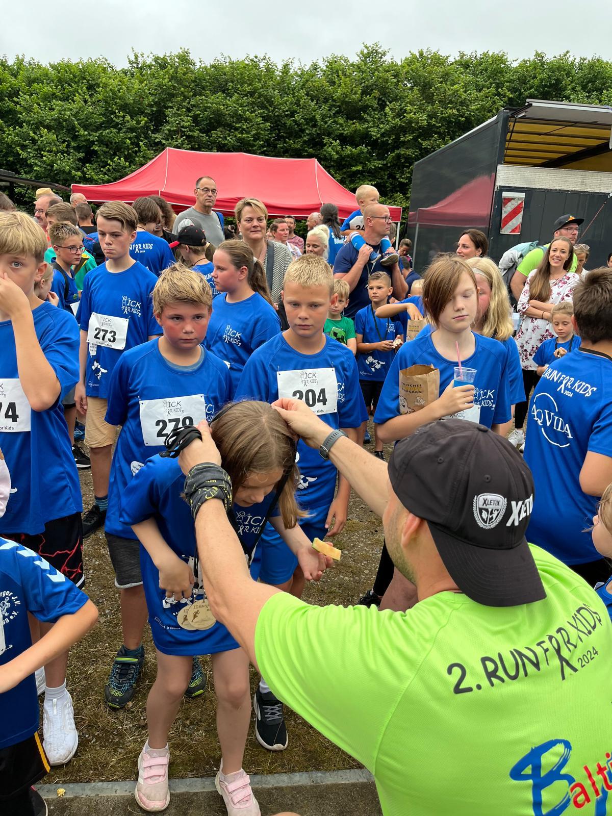 Kinder in blauen Run-for-Kids-Trikots erhalten ihre Startnummern vor dem Lauf