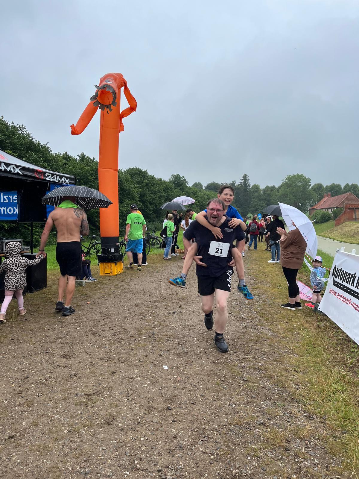 Vater trägt seinen Sohn huckepack beim Zieleinlauf des Run for Kids – gemeinsam ins Ziel